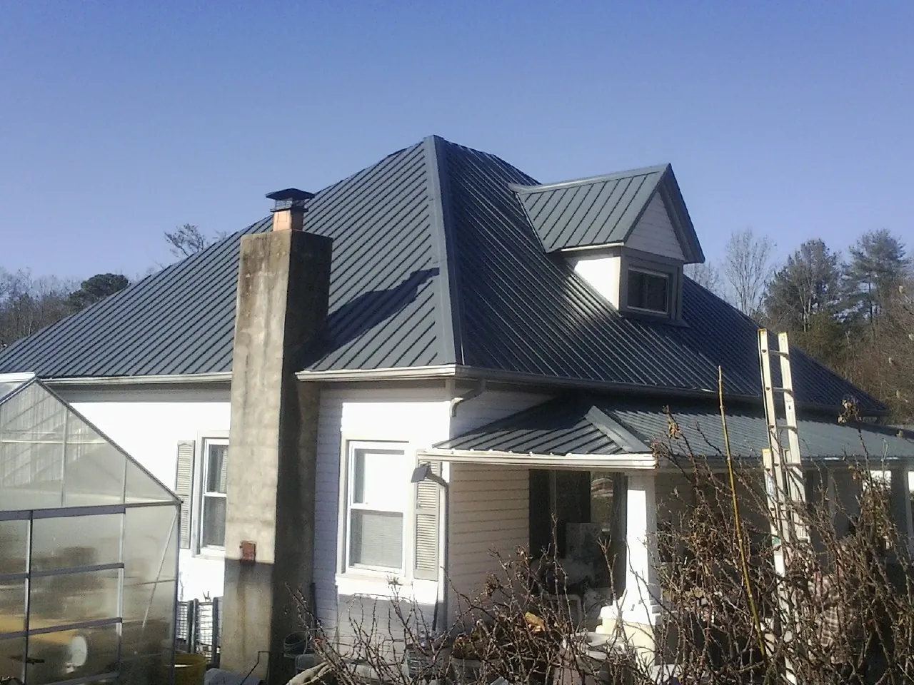 Dark blue standing seam metal roof on a white farmhouse with dormer — Slate & Tile Roof Repair by Roofing Brothers in Betterton