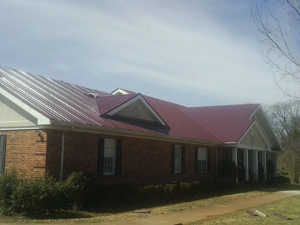 Red metal roof with gabled entries on a long brick building, from a Hail Damage Roof Repair job in Betterton