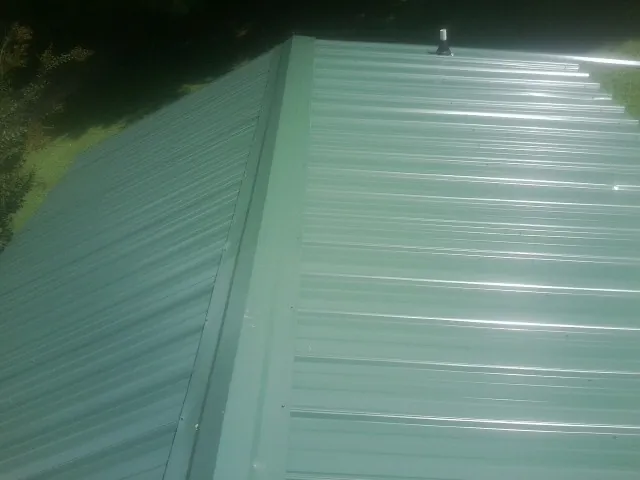 New green metal panels meeting at the ridge of a roof — Flat Roof Repair work by our crew in Betterton