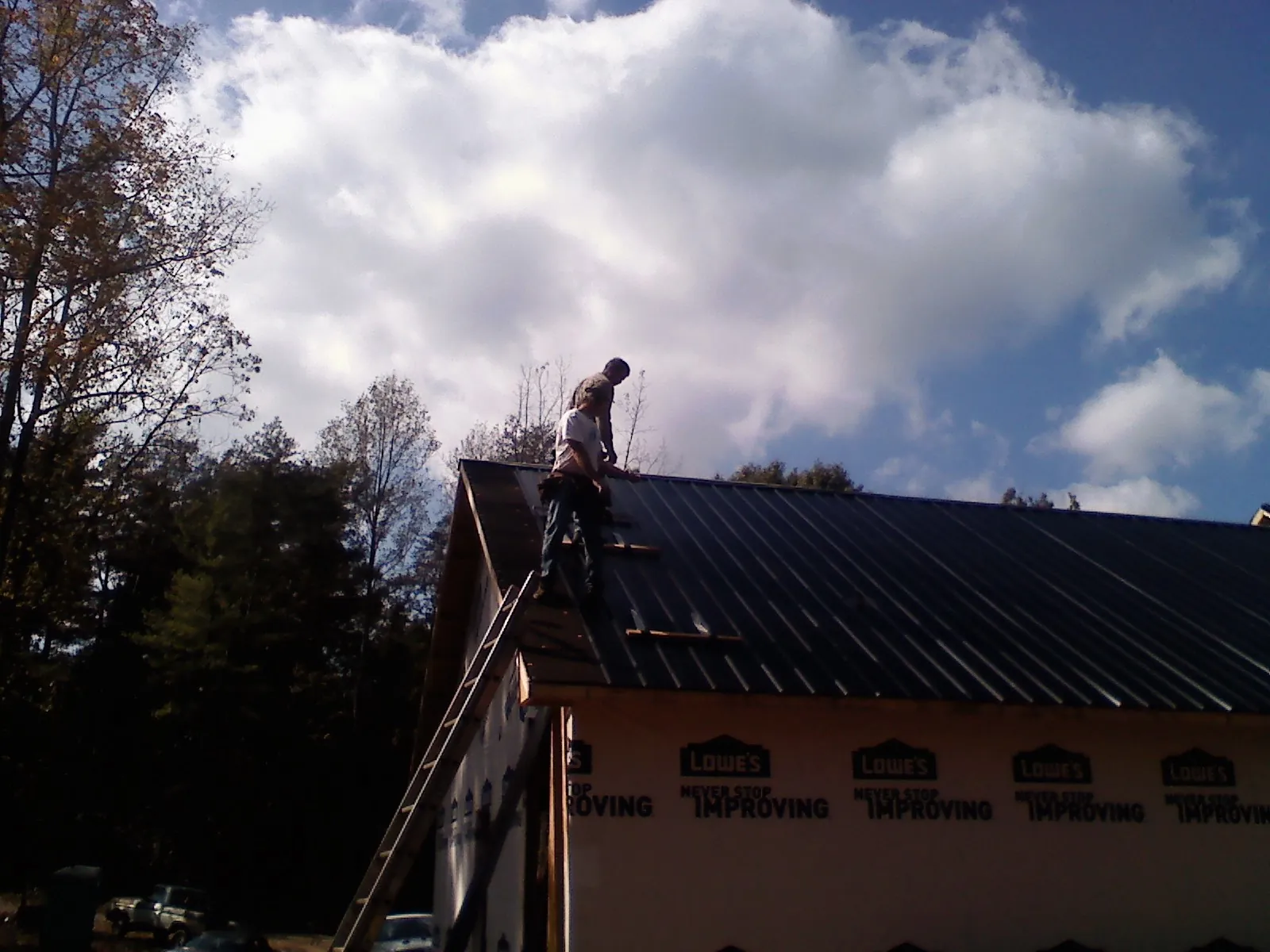 Roofer fastening dark metal panels high against a cloudy sky, from a Roof Inspection job in Betterton