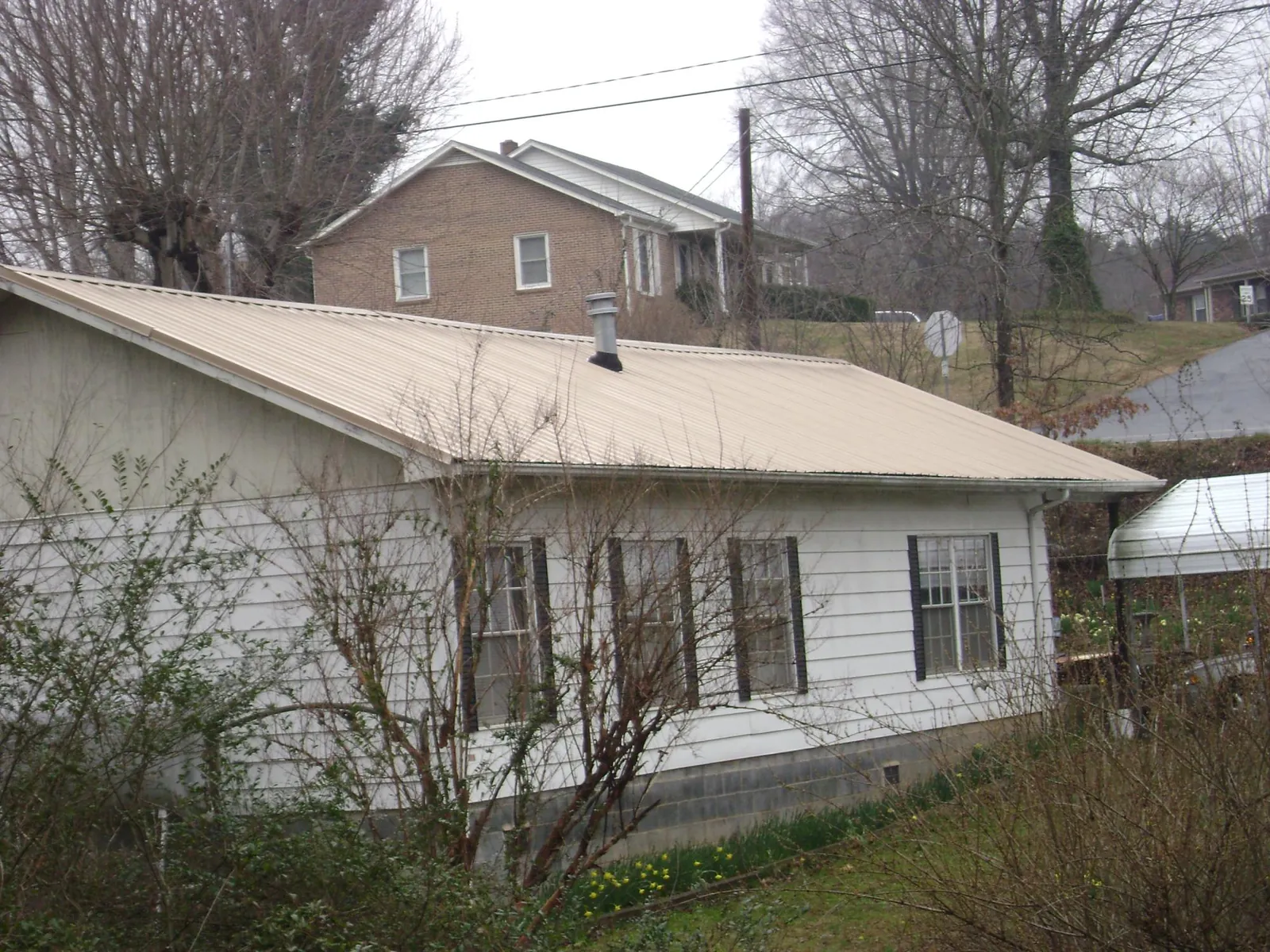 Tan metal roof on a white sided house set into a hillside — Commercial Roofing by Roofing Brothers in Betterton